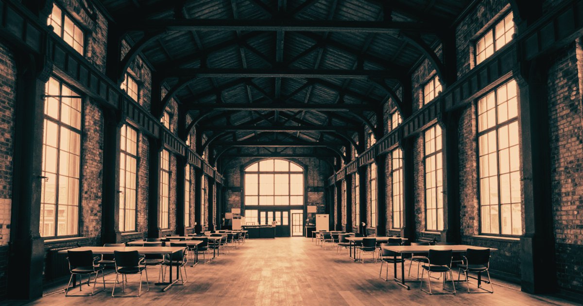 The interior of a large industrial building repurposed as a workspace - high ceilings, exposed beams, strong architectural geometry