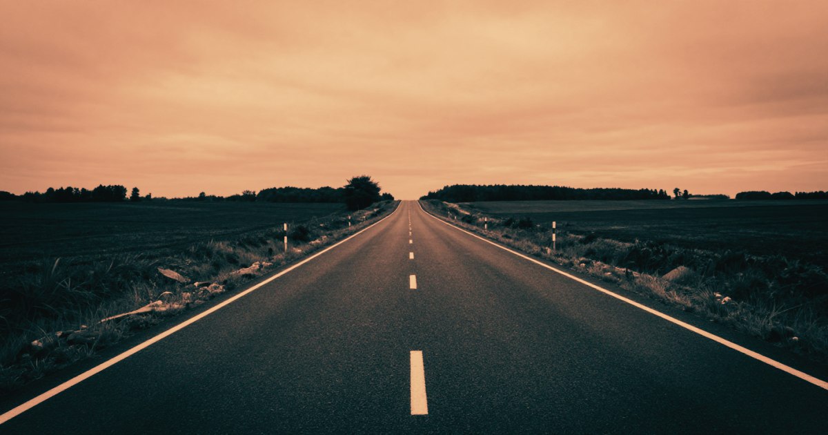 A long straight empty road shot from ground level, vanishing point in the centre