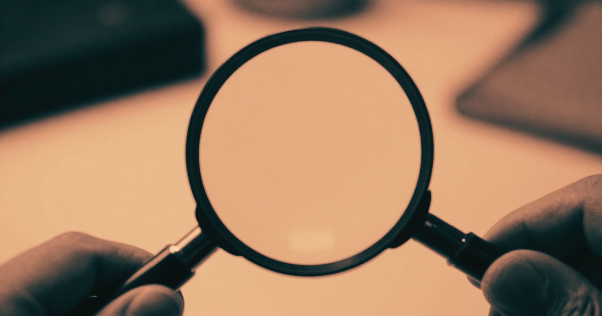 A jeweller's loupe held over a surface, sharp focus on the lens, only the hand and loupe visible