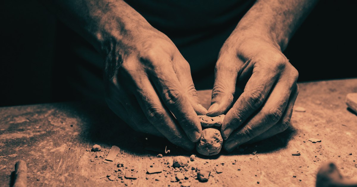 A sculptor's hands working on clay, close crop, debris around the work from material being removed