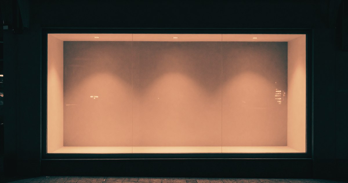 A shop window at night, lit from inside, empty interior visible through the glass