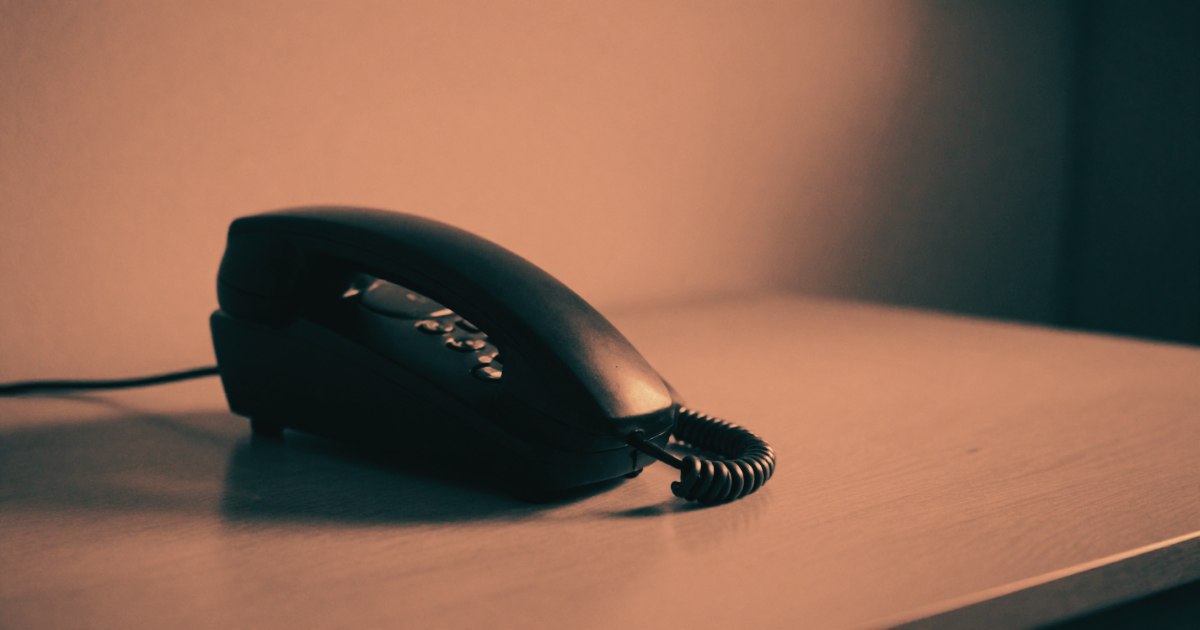 A single landline telephone handset resting off its cradle on a bare desk