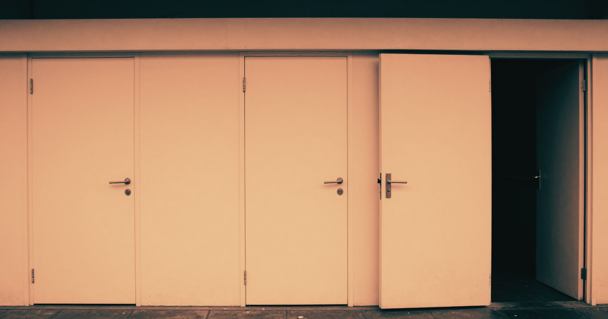 A long row of identical doors in a corridor, all closed, one door at the end slightly different and ajar