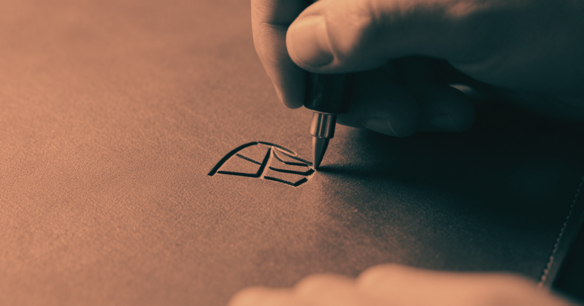 A craftsman's hand carving a unique mark into material - deliberate differentiation, a mark that belongs to one person