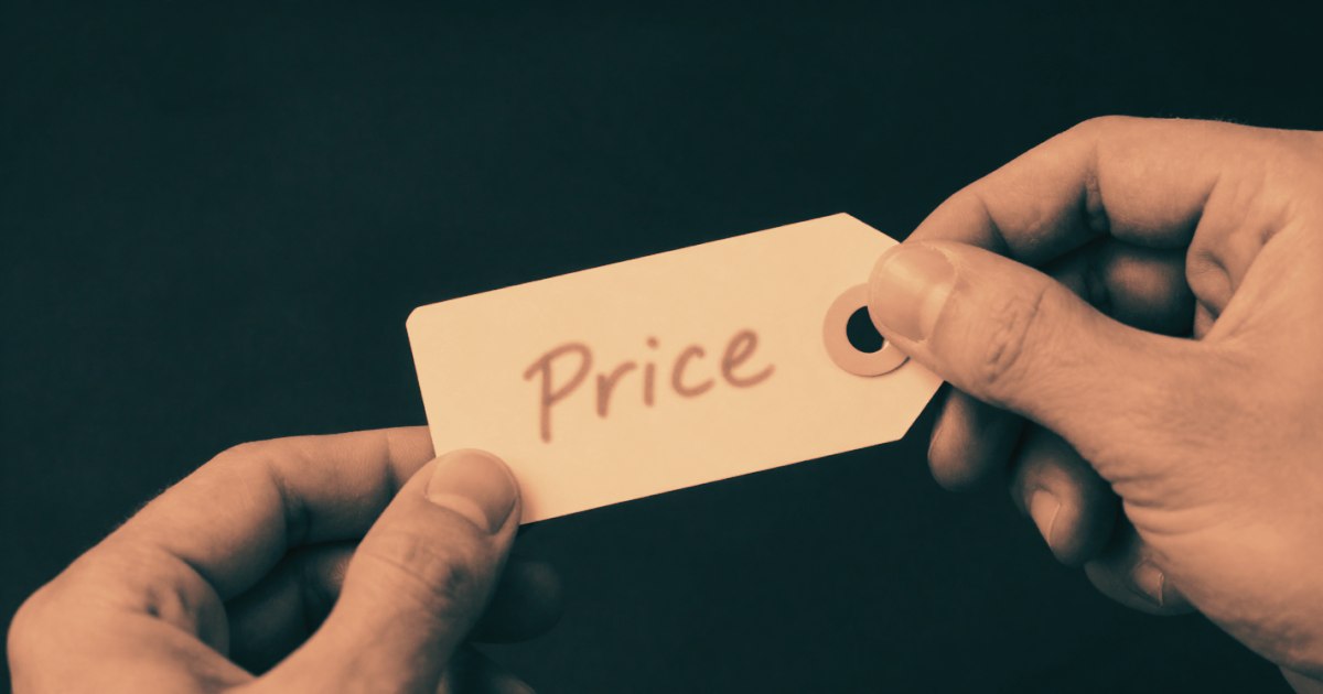 Hands holding a small handwritten price tag, close crop, the number deliberately blurred