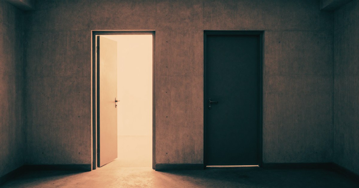 Two identical doors side by side in a stark concrete corridor - one open, one closed